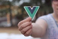 Close-up of a person holding a Vue.js logo sticker outdoors during springtime.