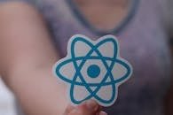 A person holds a sticker featuring the React logo, commonly used in web development.