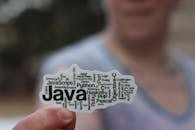Close-up of a person holding a sticker with various programming languages listed on it.